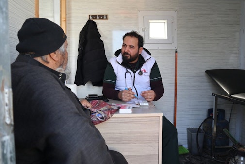 Een Syrische man is in gesprek met onze arts tijdens een consultatie in onze mobiele kliniek in het kamp Qadimoon