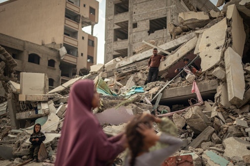 Een vrouw en haar kinderen zoeken naar hun spullen onder het puin in Gaza-Stad.