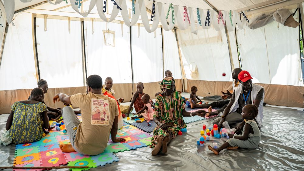 Families en therapeuten spelen met blokken tijdens een speltherapiesessie. Speltherapie vindt plaats in een stimulerende omgeving en is een aanvulling op medische en voedingszorg.