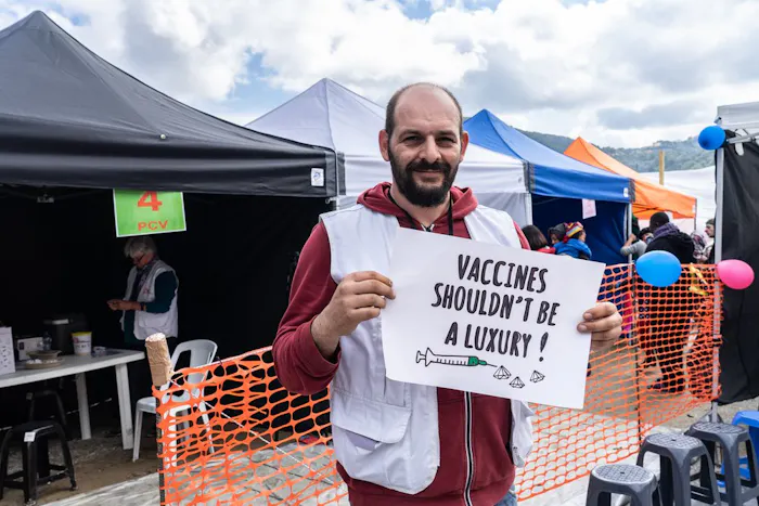 Athanasios is onze logistiek medewerker in Griekenland. Hij houdt een bord waarop staat: vaccins zouden geen luxe moeten zijn