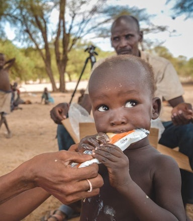 Vrijwilliger Artsen zonder Grenzen geeft pindapasta aan ondervoed kind Kenia