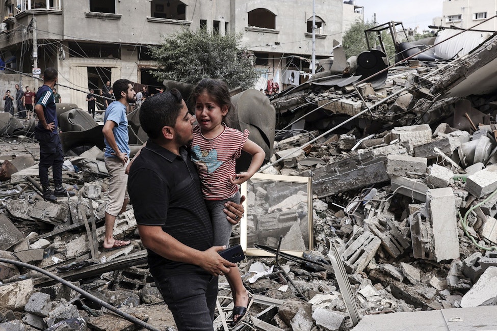 Een man draagt een huilend kind voor een gebouw verwoest door een Israëlische luchtaanval in Gaza-Stad.