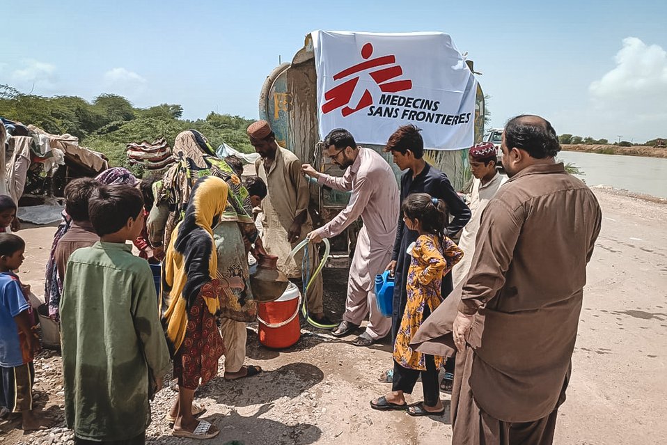 Medewerkers van Artsen zonder Grenzen bieden wachtende mensen schoon drinkwater aan via een watertank.
