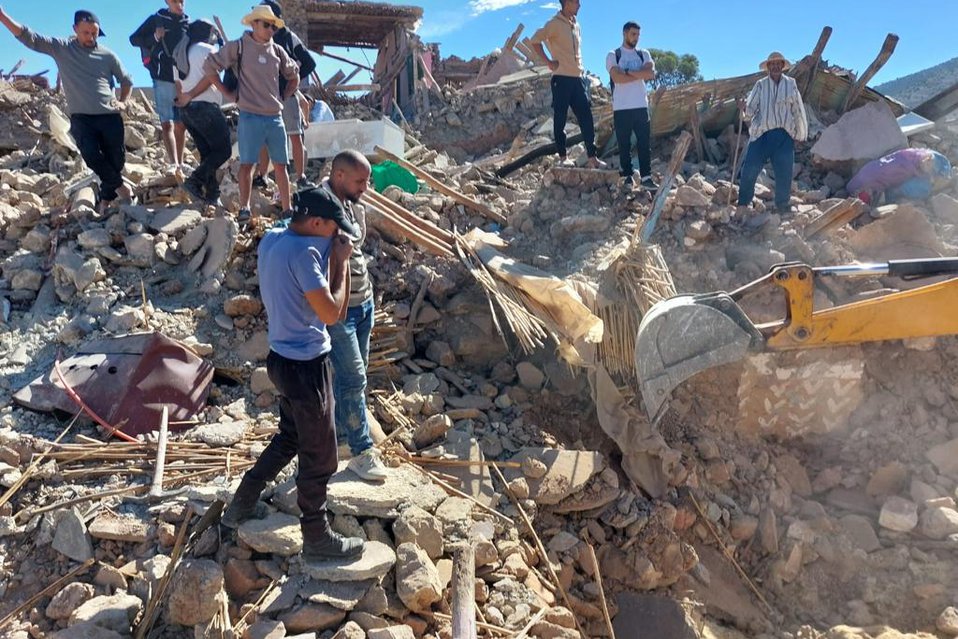 Een groep mensen kijkt naar een graafmachine die in het puin graaft na een aardbeving in Marokko.