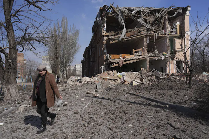 Een vrouw loopt langs een gebouw dat geraakt is door beschietingen. Mariupol, Oekraïne, 13 maart 2022