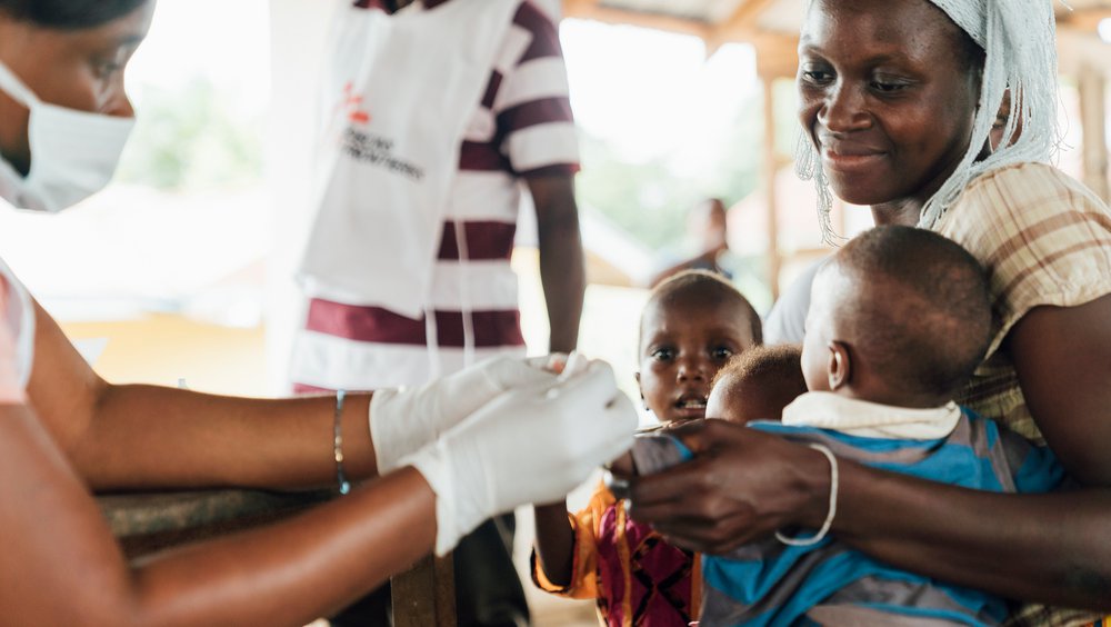 Een medewerker van Artsen zonder Grenzen helpt een vrouw en haar kinderen in een ziekenhuis in Sierra Leone.