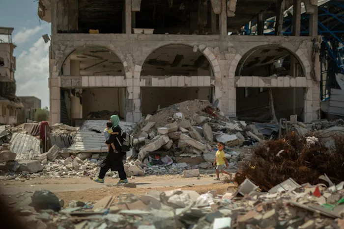 Een vrouw loopt met een kind door een verwoeste straat in Gaza.