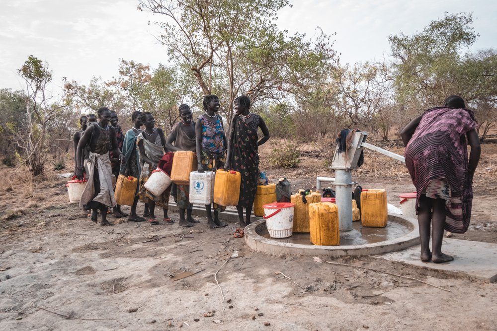 Vrouwen in het dorp Akelo, Labarab, staan te kletsen, terwijl ze wachten op hun beurt om water uit het boorgat te halen.
