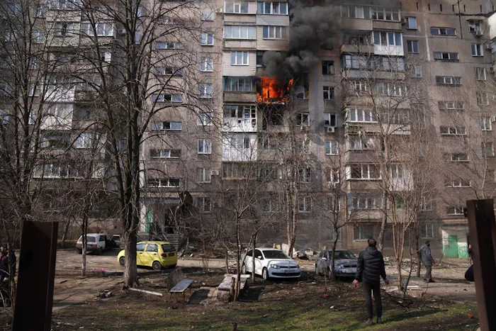 Mensen kijken naar een brandend flatgebouw na beschietingen in Mariupol, Oekraïne
